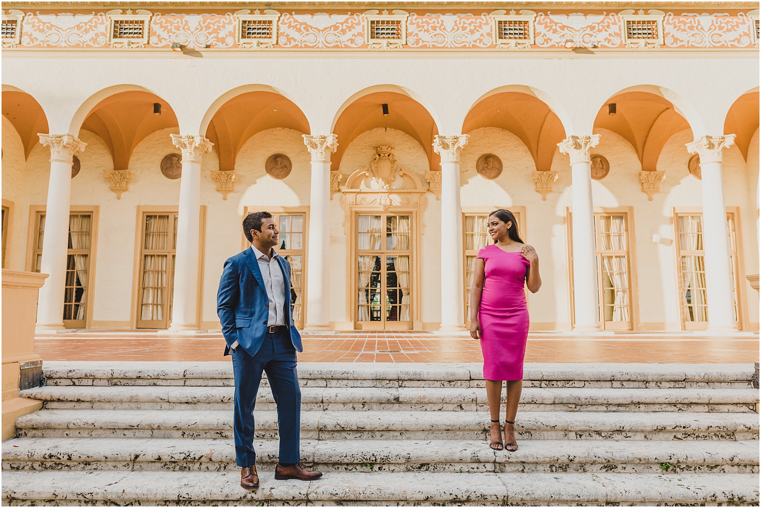 A couple walking around the Biltmore Hotel in Coral Gbles, FLorida taking their engagement photos dressed un a blue suite and pink dress.