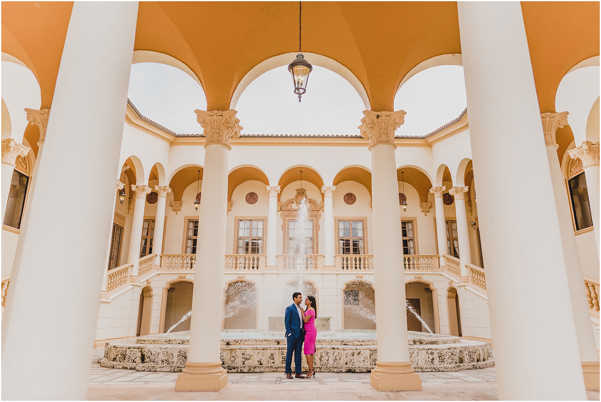 A couple walking around the Biltmore Hotel in Coral Gbles, FLorida taking their engagement photos dressed un a blue suite and pink dress.