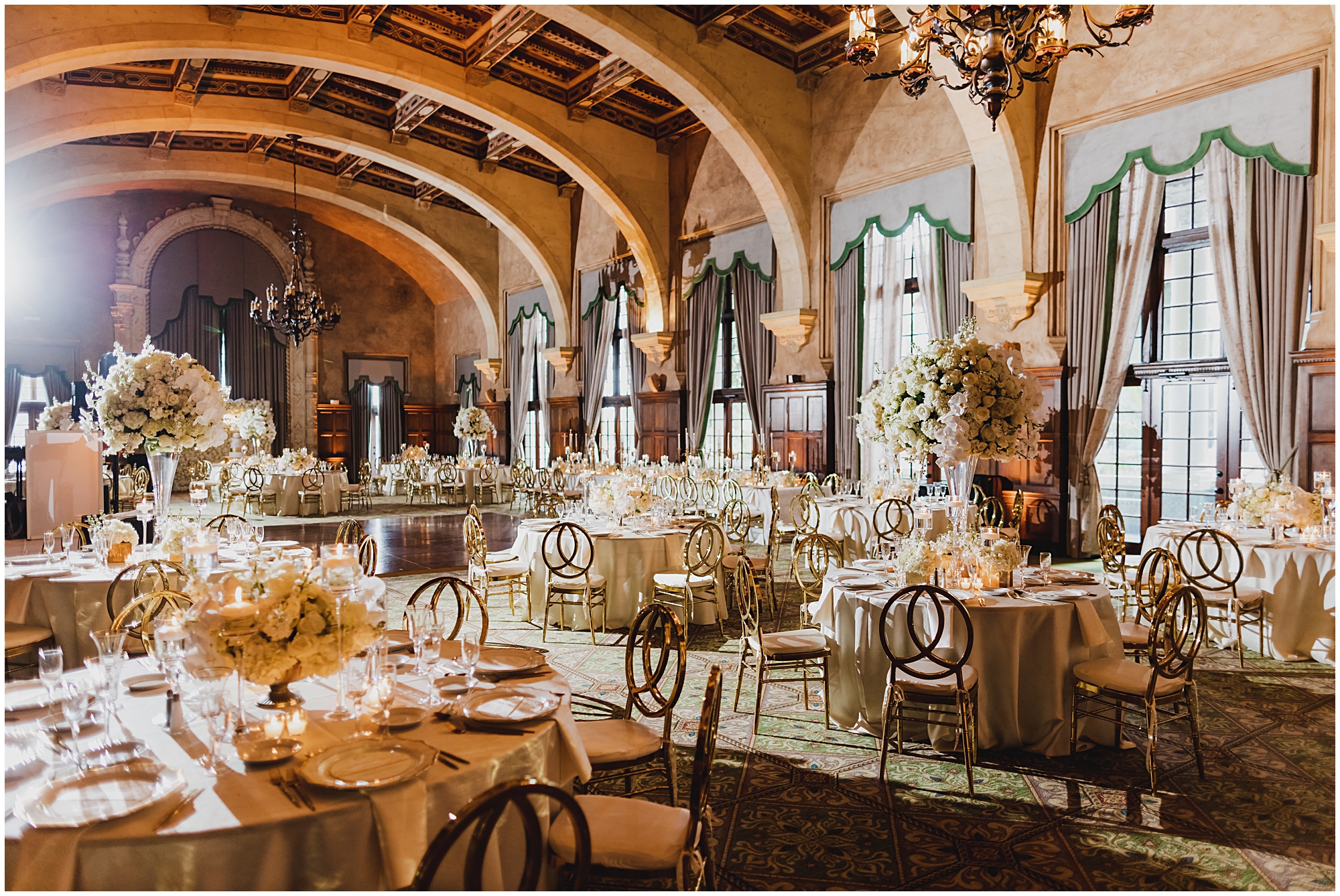 Wide photo of the Alhambra ballroom at the Biltmore Hotel with infinity gold chairs, white linens, white orchid florals and hydrangeas. 