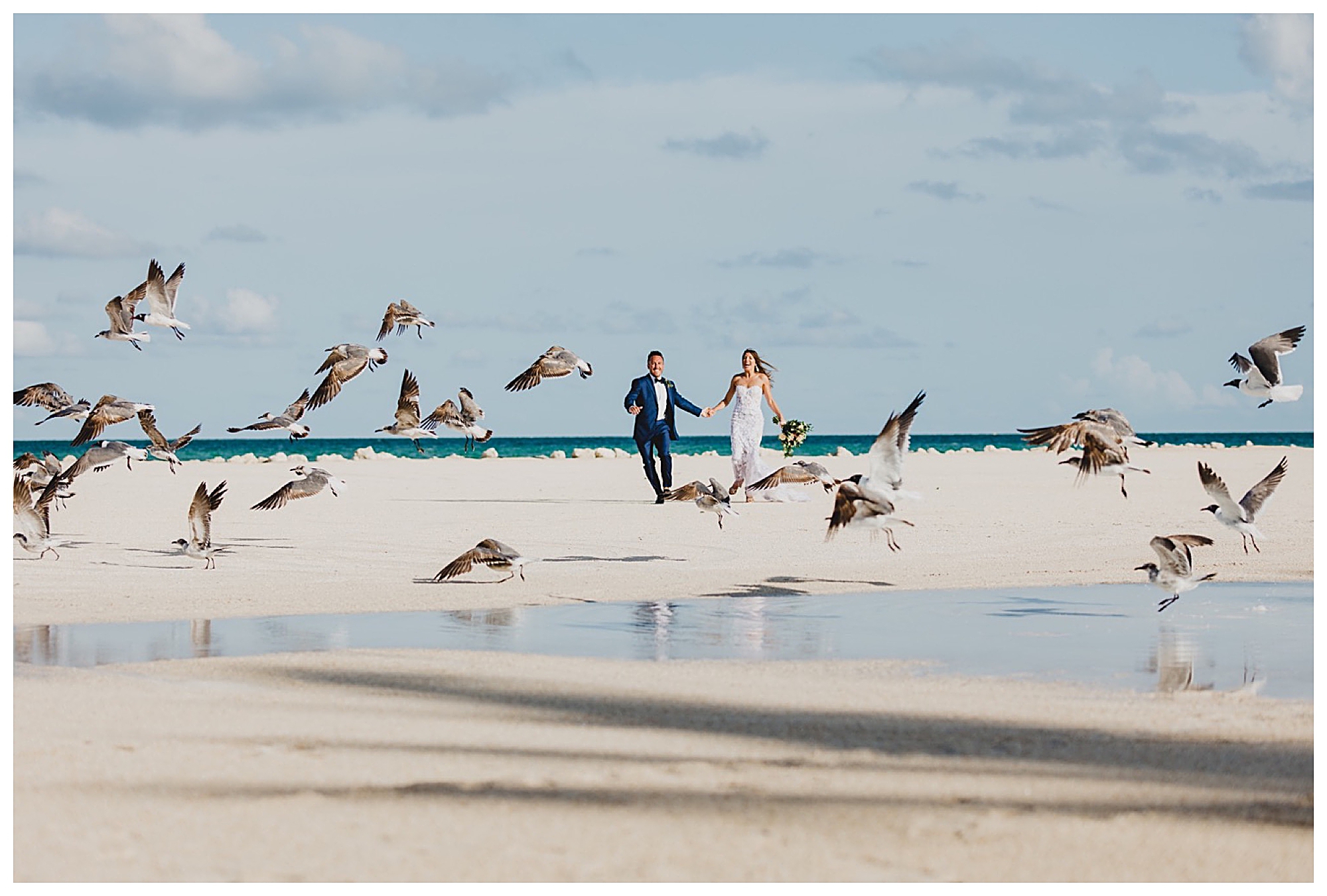 bride and groom running across the beach with birds flying around them